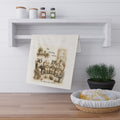 A cream-colored kitchen towel with a vintage-style illustration of knitting ewes and the text 'The Knitting Circle' hanging from a white wall rack in a bright kitchen setting.